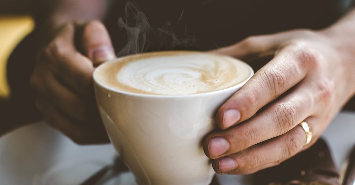 Tasse Kaffee auf einem Nachttisch neben einem Wecker und einem Bett
