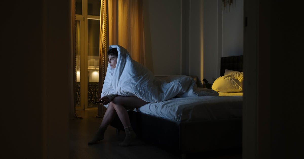 Person liegt wach im Bett und schaut auf den Wecker auf dem Nachttisch